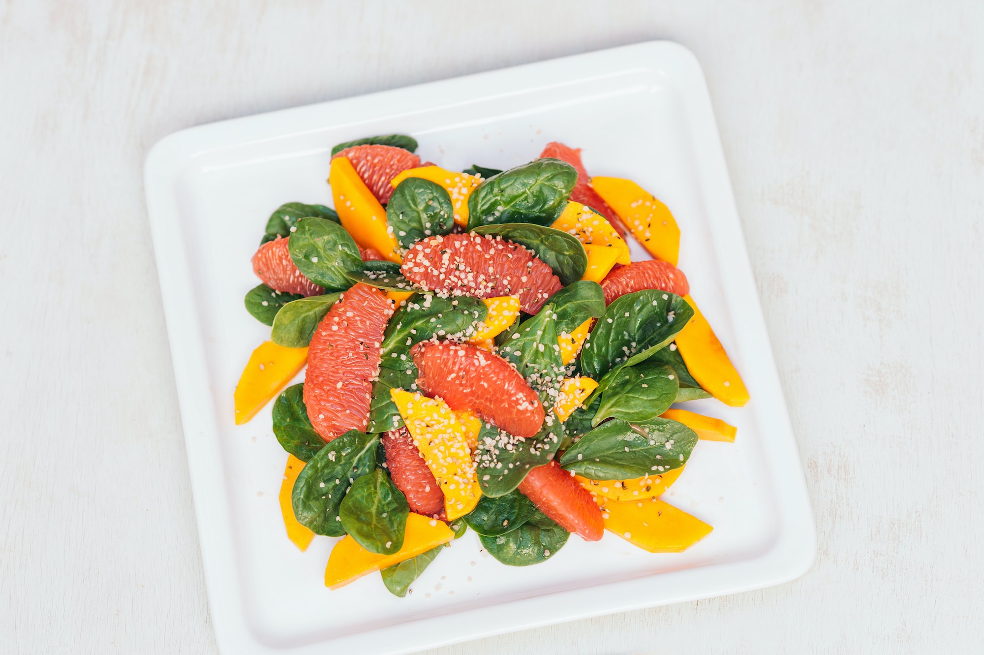 Fresh salad of mango, grapefruit, spinach and hempseed on white square plate