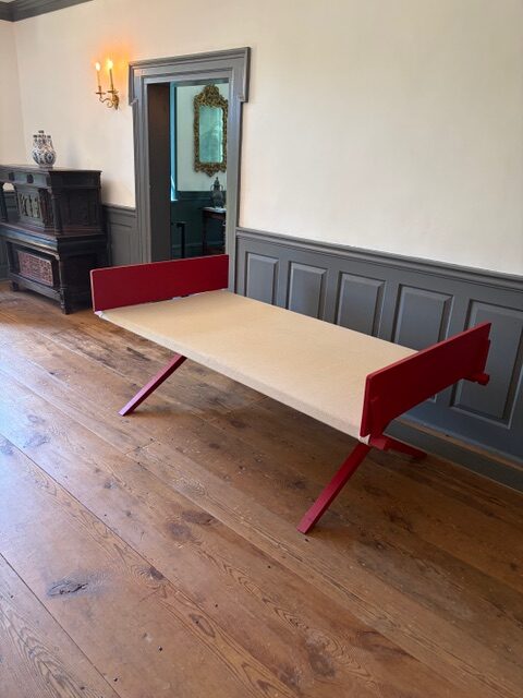 Reproduction 18th-century hemp canvas camp bed with a red folding frame in a paneled room at the Dey Mansion